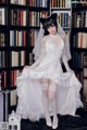 A woman in a wedding dress sitting in front of a bookshelf.