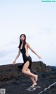 A woman in a black dress standing on a rocky beach.