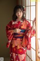 A woman in a red kimono leaning against a window.