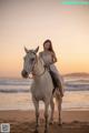 A woman in a white dress riding a white horse on the beach.