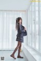 A woman in a school uniform standing by a window.