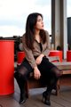 A woman sitting on a wooden bench wearing a leopard print jacket.