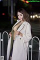 A woman in a white coat standing next to a fence.