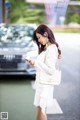 A woman in a white dress is looking at her phone.